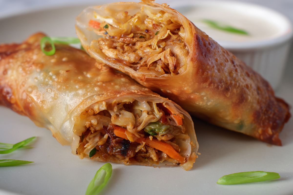 Crispy egg rolls cut in half, revealing a filling of shredded chicken, cabbage, carrots, and green onions on a white plate.