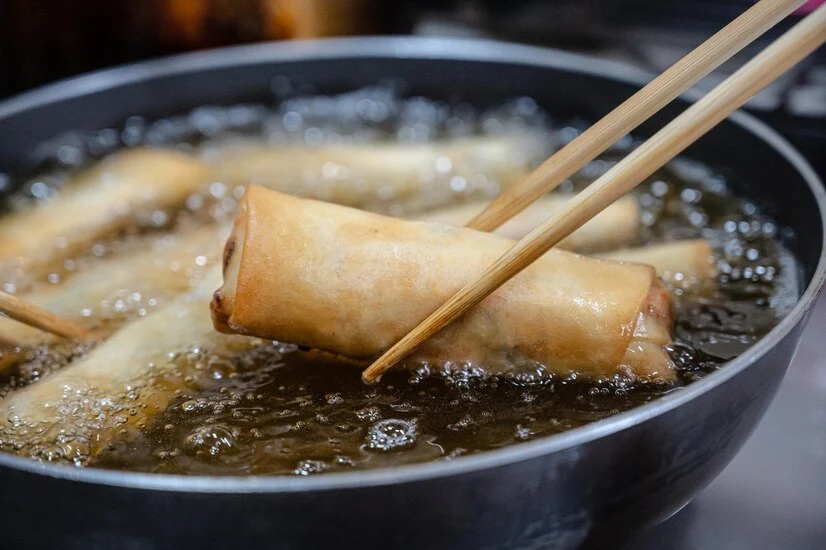 Golden fried egg rolls in a skillet with vegetable oil