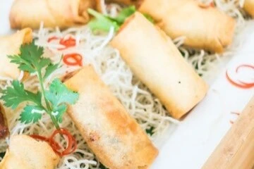 Golden fried egg rolls in a skillet with vegetable oil