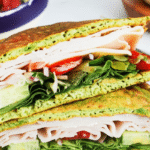 Sandwich made with vibrant green avocado bread, turkey slices, fresh spinach, cucumber, tomatoes, and onions.